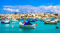 Barche colorate nel porto di Malta con case sullo sfondo.