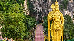 Statua dorata di Murugan davanti alle grotte di Batu, circondata da vegetazione.