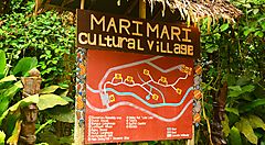 Cartello turistico al Mari Mari Cultural Village immerso nella vegetazione.
