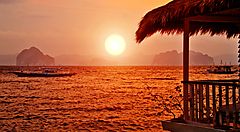 Tramonto sul mare a Bali con una barca all'orizzonte.