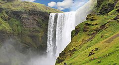 Cascata islandese circondata da paesaggio verde e roccioso.