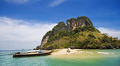 Spiaggia tropicale con barca e vista su formazione rocciosa a Phuket.