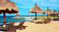 Spiaggia tropicale di Bali con ombrelloni di paglia e lettini.