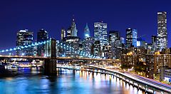 Skyline notturno di New York con grattacieli illuminati e ponte.