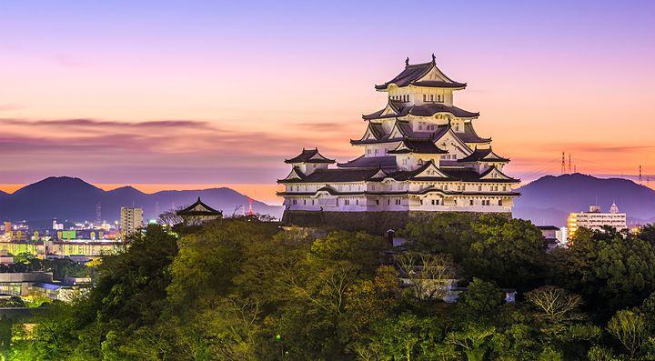 Il Castello di Himeji al tramonto con sfondo di montagne.