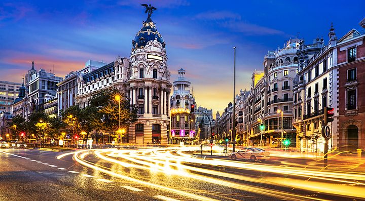Gran Via di Madrid illuminata al tramonto con traffico in movimento.
