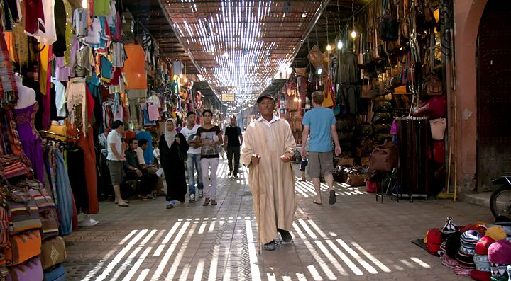 Mercato coperto in Marocco con persone che camminano e bancarelle colorate.