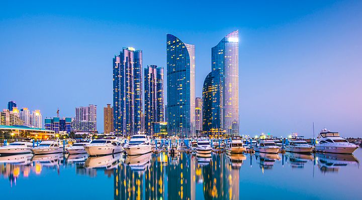 Grattacieli moderni e yacht nel porto di Busan al tramonto.