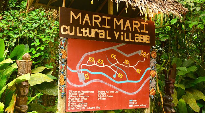 Cartello turistico al Mari Mari Cultural Village immerso nella vegetazione.