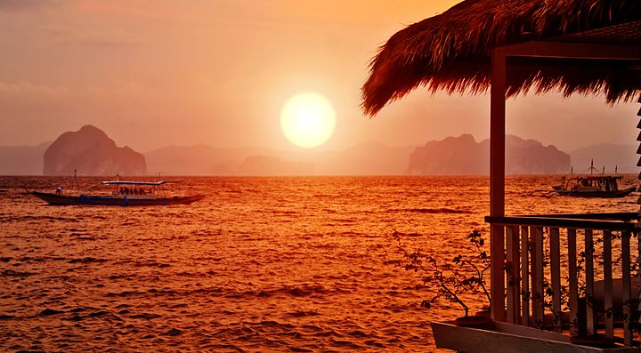 Tramonto sul mare a Bali con una barca all'orizzonte.