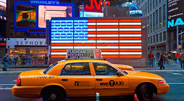 Taxi giallo a New York davanti a una bandiera americana luminosa.