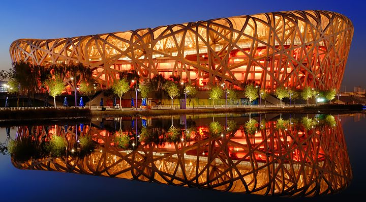 Lo Stadio Nazionale di Pechino illuminato di sera, riflesso nell'acqua.