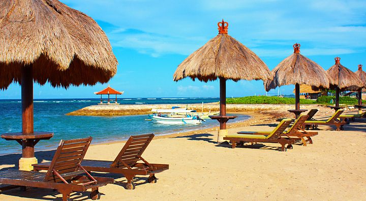 Spiaggia tropicale di Bali con ombrelloni di paglia e lettini.