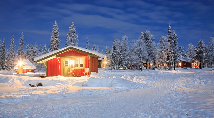 Casetta rossa nella neve svedese, circondata da alberi sotto un cielo blu notturno.