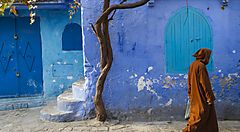 Strada di Chefchaouen in Marocco con muri blu e persona in abito tradizionale.