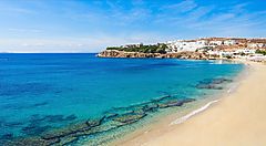 Spiaggia di sabbia dorata a Mykonos con mare azzurro e cielo sereno.