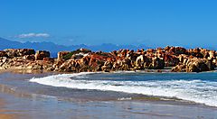 Spiaggia rocciosa in Sudafrica con onde e cielo azzurro.