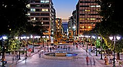 Viale illuminato ad Atene con persone che passeggiano di sera.