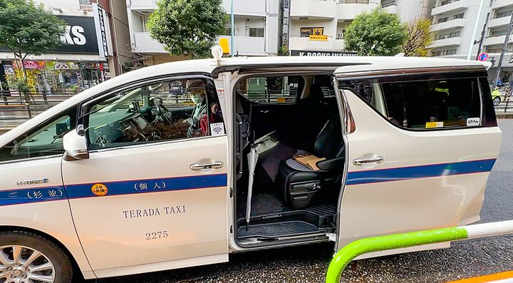 Taxi bianco fermo su strada cittadina con porta aperta.