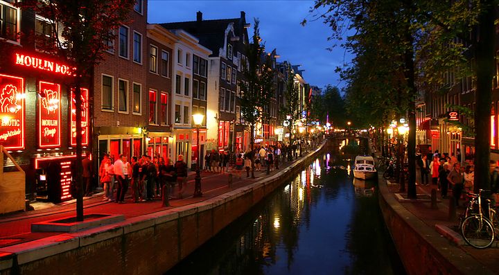 Canale illuminato di notte ad Amsterdam con locali e persone.