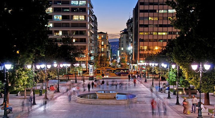Viale illuminato ad Atene con persone che passeggiano di sera.