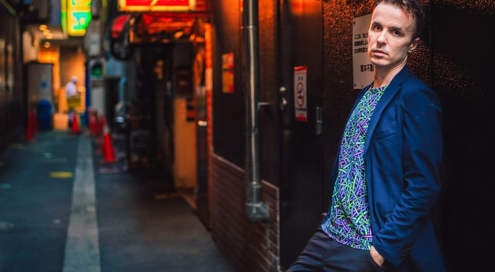 Marco Togni posa in un vicolo a Tokyo la sera.
