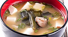 Zuppa di miso con tofu, alghe e cipollotto in una ciotola rossa e nera.
