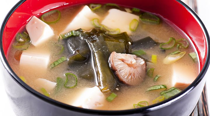 Zuppa di miso con tofu, alghe e cipollotto in una ciotola rossa e nera.