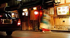 Strada notturna nel quartiere di Gion, Kyoto, con lanterne e figure in movimento.