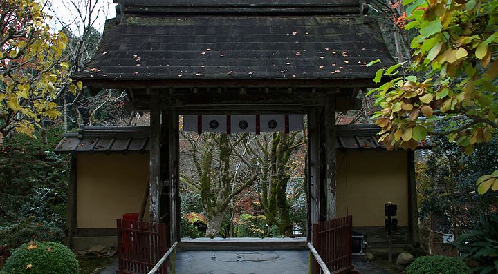 Ingresso di un giardino giapponese con portale in legno e vegetazione attorno.