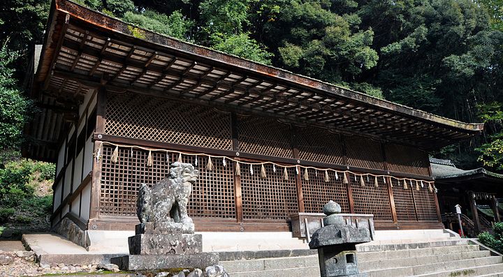 Edificio tradizionale in legno e pietra circondato da alberi e statue in pietra.