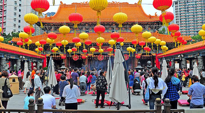 Il tempio di Wong Tai Sin, con lanterne gialle e rosse, e molte persone durante una celebrazione.