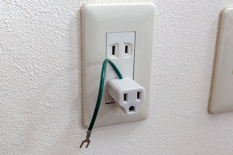 Un adattatore elettrico bianco inserito in una presa a muro giapponese su una parete ruvida.
