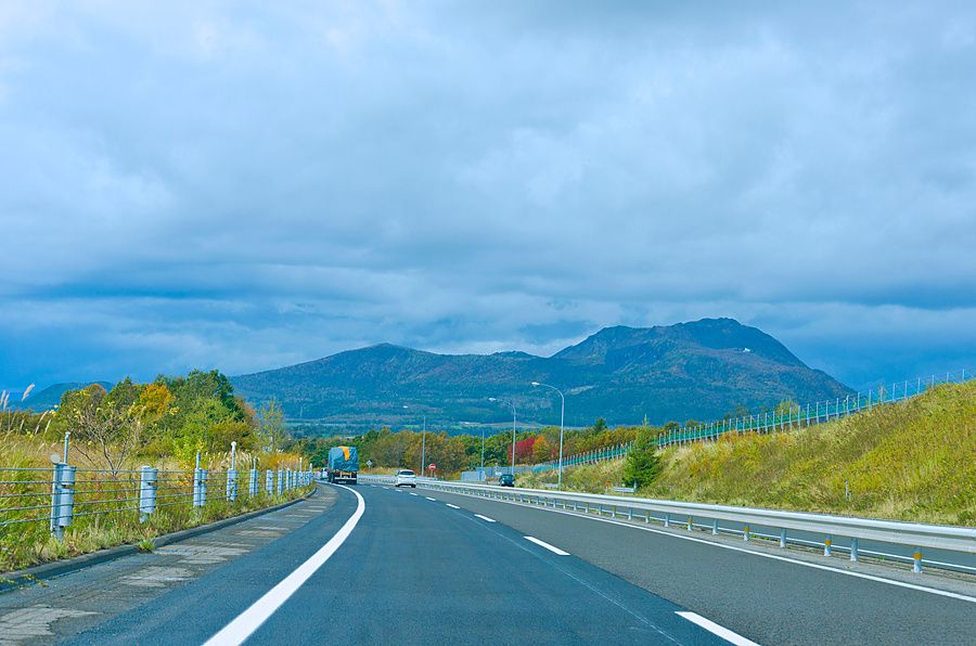 Veduta frontale di un'autostrada in Hokkaido con in primo piano la segnaletica orizzontale e sullo sfondo il monte Usu.