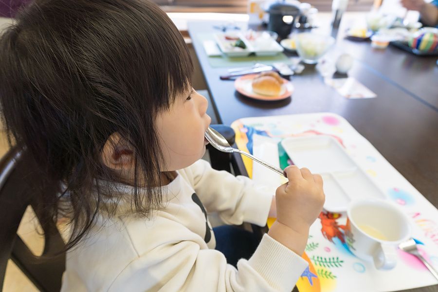 Una bambina asiatica con capelli scuri mangia con un cucchiaio in un contesto interno.