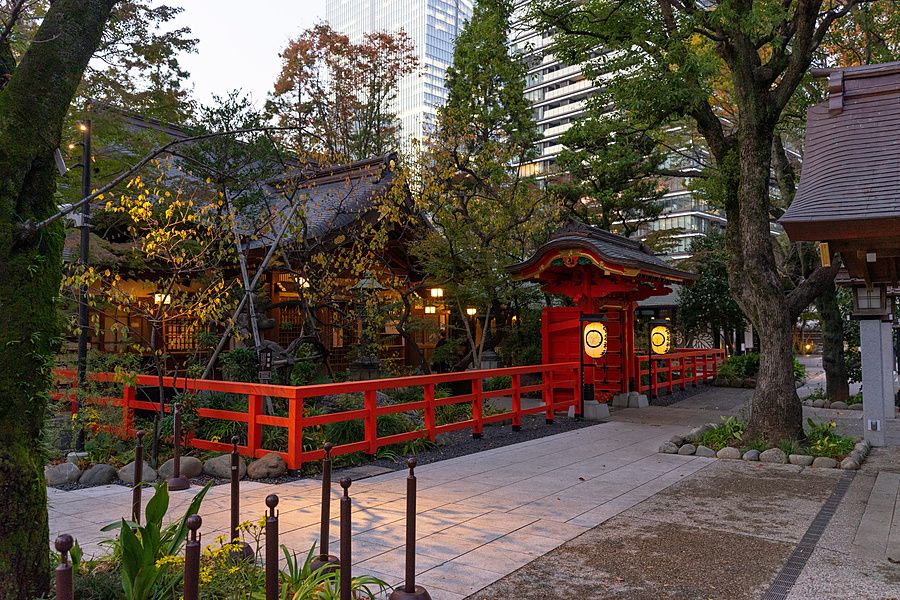 Cancello karamon rosso del santuario Atago a Tokyo circondato da alberi e edifici moderni.