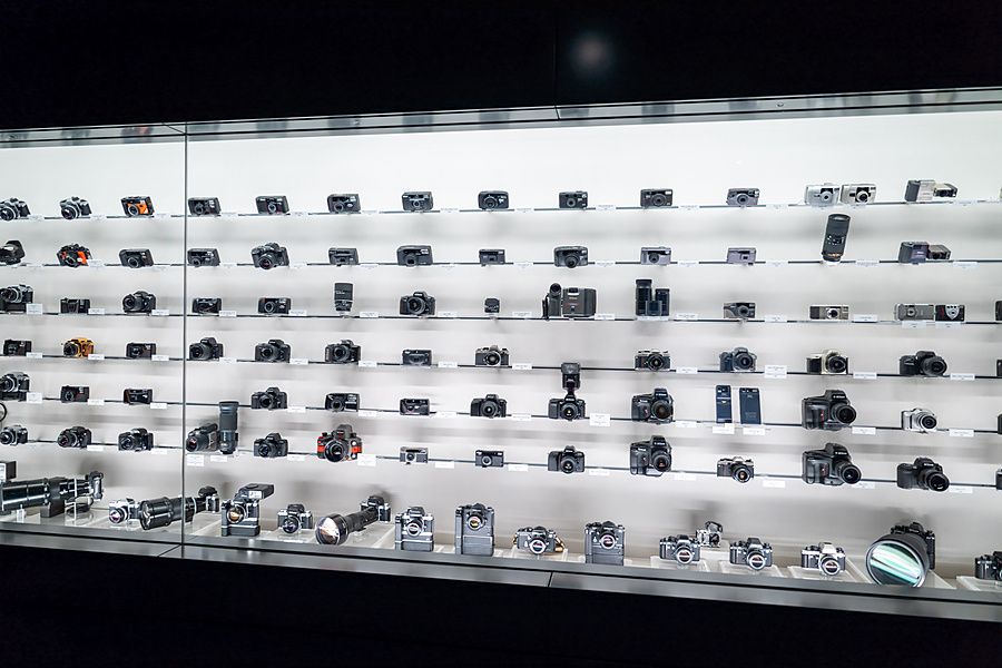 Parete espositiva di numerose fotocamere storiche Nikon disposte su scaffali illuminati in un museo.