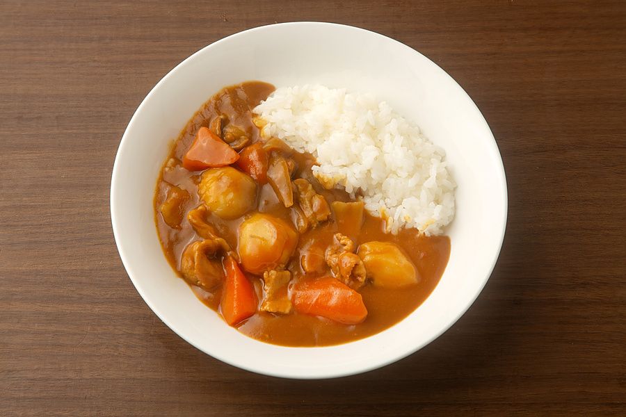 Piatto di curry giapponese con riso bianco e pezzi di carote e carne servito su un tavolo in legno.
