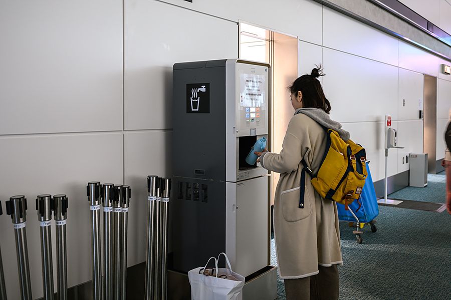 Donna riempie una borraccia azzurra in un distributore d'acqua automatico all'interno di un aeroporto di Tokyo.