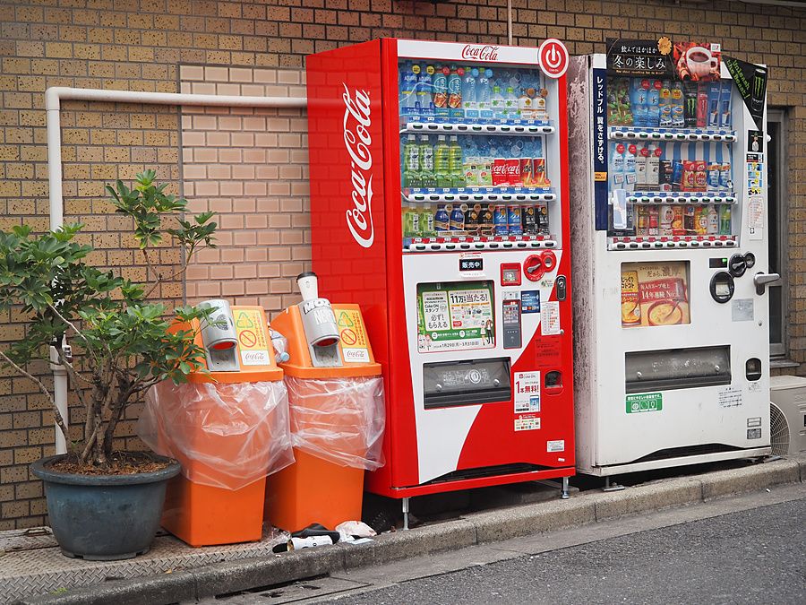 Due distributori automatici di bevande su un marciapiede a Shibuya, Tokyo, con accanto cestini per il riciclo.