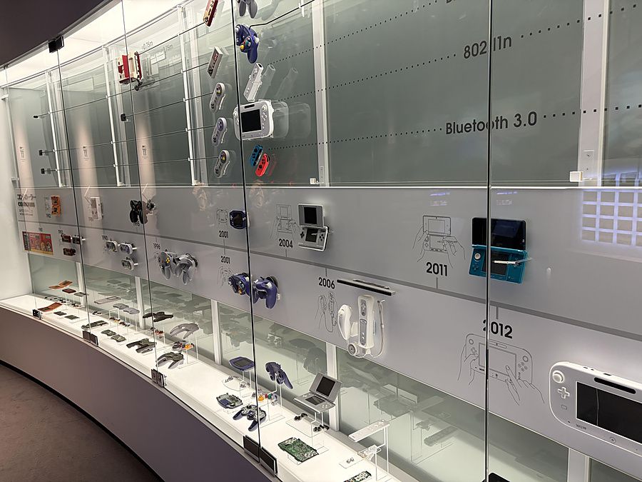 Vetrina espositiva del Nintendo Museum a Kyoto con console e controller storici disposti cronologicamente.