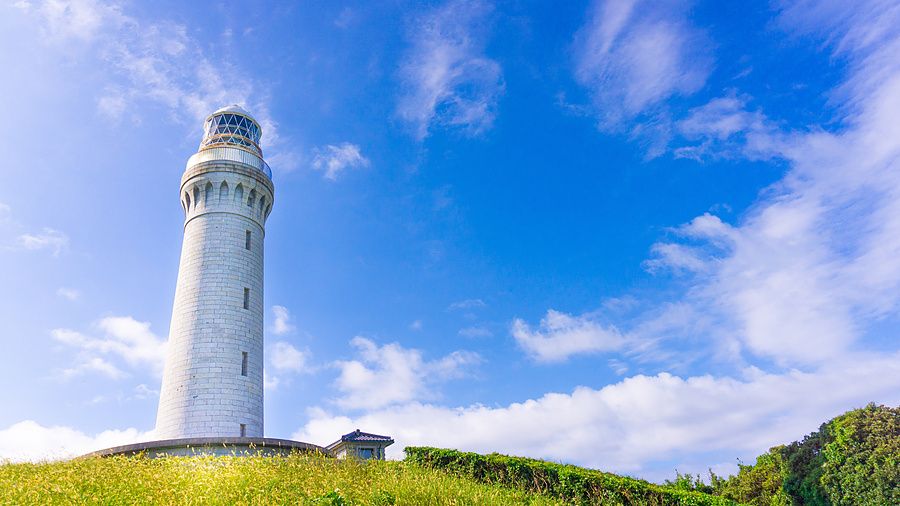 Il faro di Tsunoshima bianco si staglia contro un cielo azzurro luminoso sopra una collina erbosa verde.