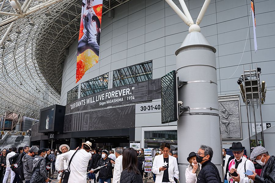 Persone in attesa davanti all'ingresso del Tokyo Dome con scritte e poster dedicati al baseball.