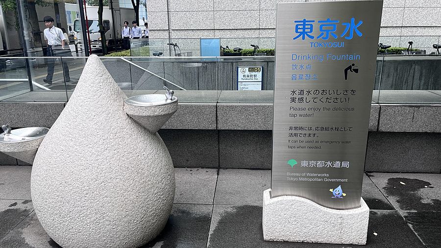 Fontanella pubblica a forma di goccia vicino a un pannello informativo in metallo a Tokyo.