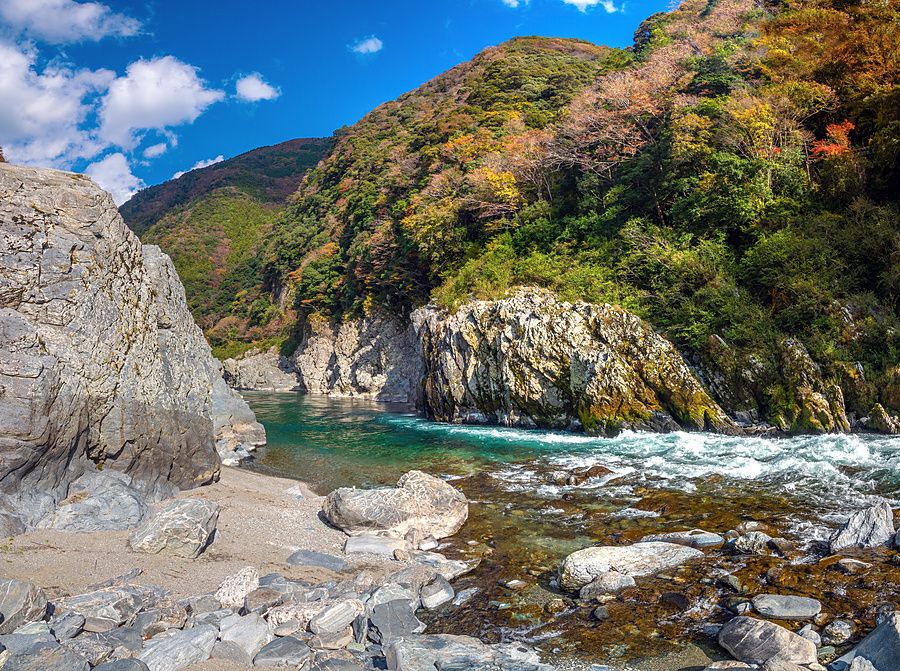 Veduta panoramica di una gola fluviale con acque turchesi tra rocce scoscese e pendii boscosi in autunno.