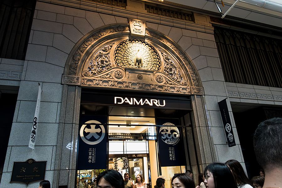 Ingresso del grande magazzino Daimaru a Osaka con bassorilievo di pavone e insegna luminosa sopra le porte.