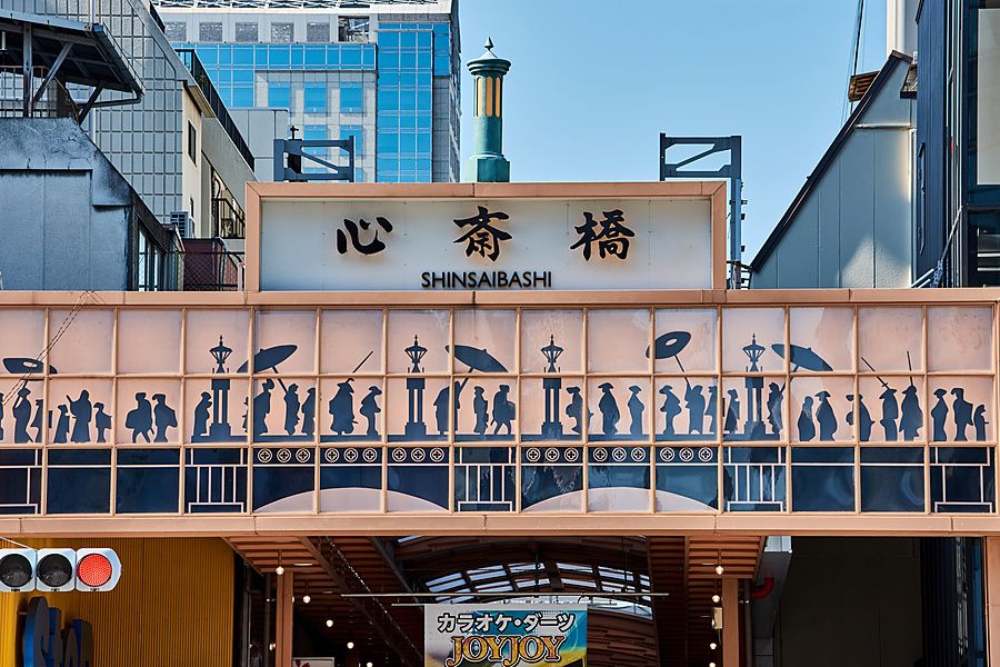 Insegna decorata dell'ingresso di Shinsaibashi a Osaka con silhouette di persone e caratteri giapponesi.