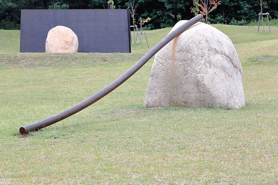 Installazione d'arte moderna con grandi pietre e una barra di ferro su un prato verde nel Lee Ufan Museum a Naoshima.