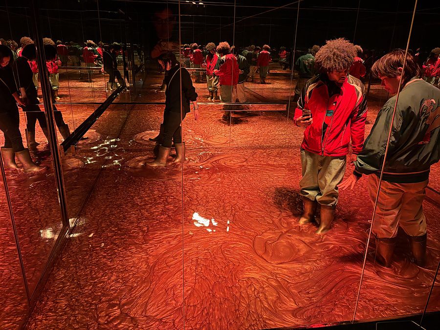 Persone esplorano un'installazione artistica immersiva con superfici rosse e specchi a Kyoto.