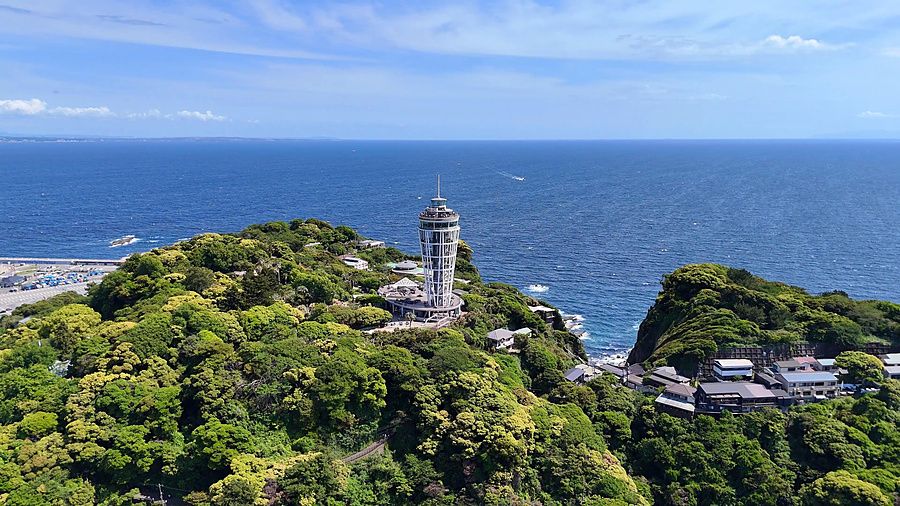 Veduta aerea panoramica dell'isola di Enoshima con il faro Sea Candle circondato dal verde e dal mare in Giappone.